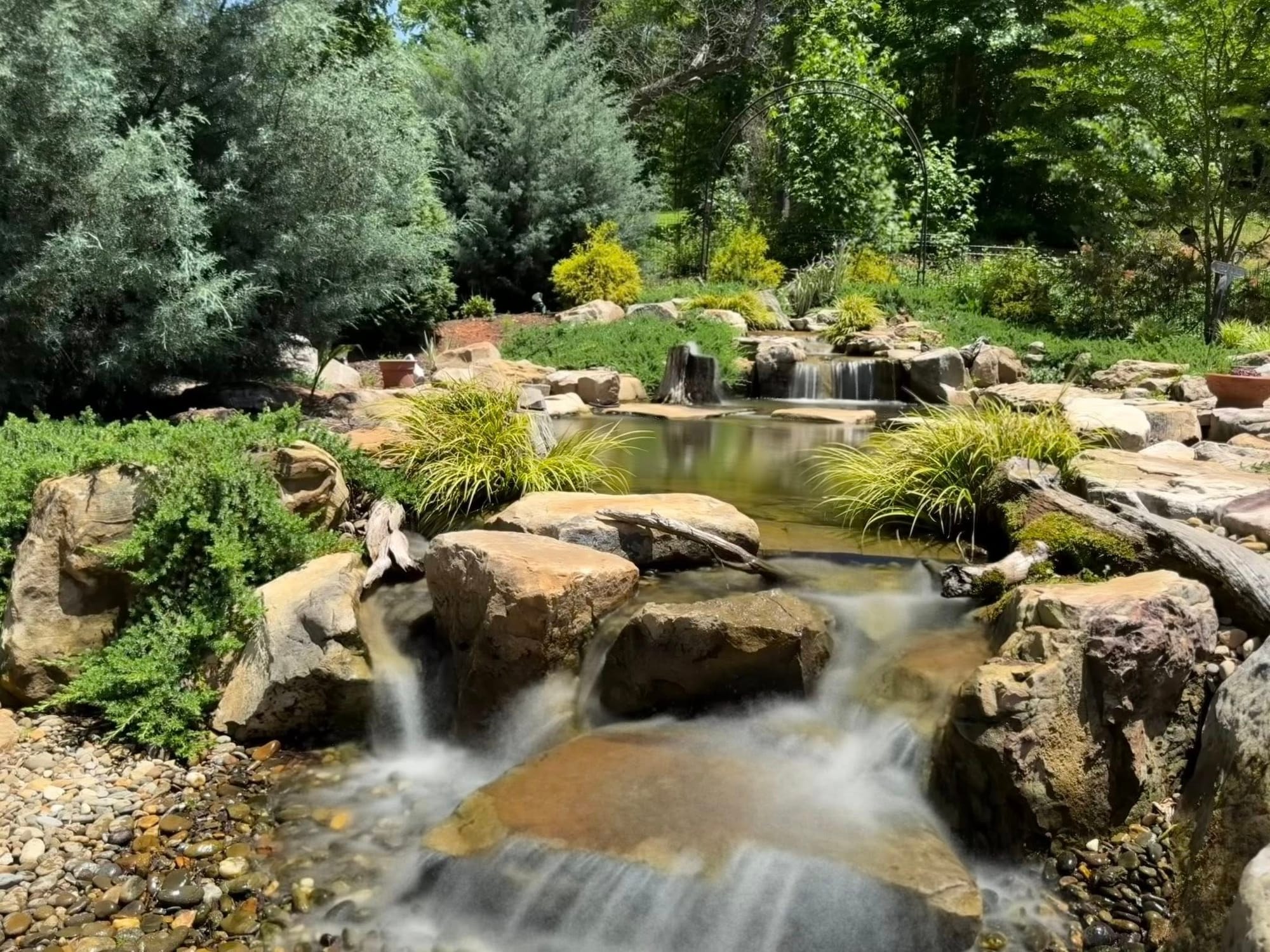 Садовий ставок із камінням, рослинами та водоспадом серед зелені