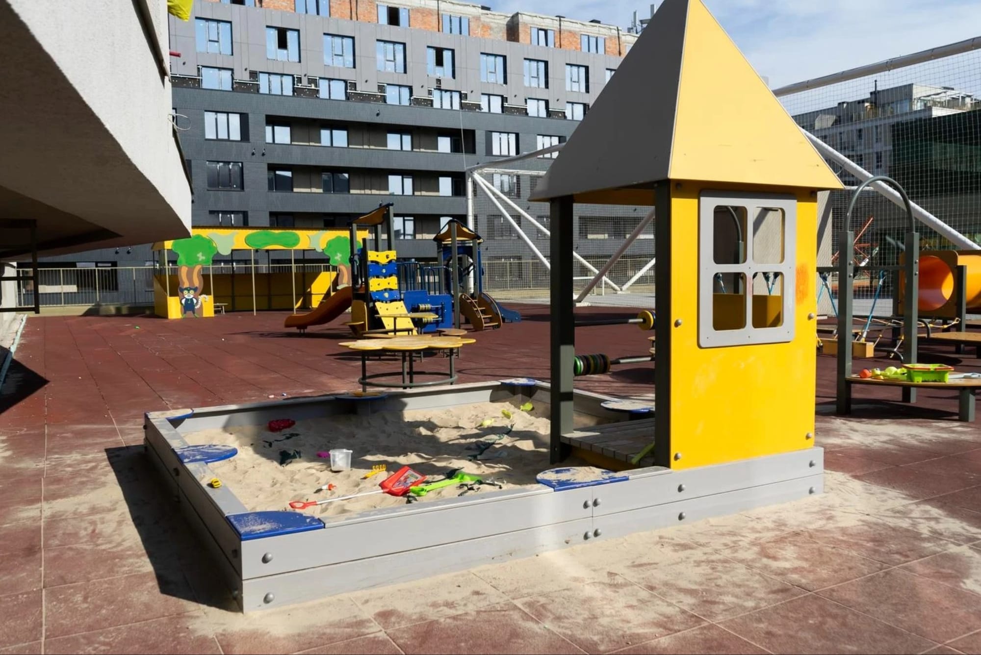 Дитячий майданчик з пісочницею, гірками та ігровими елементами на подвір’ї багатоповерхових будинків.