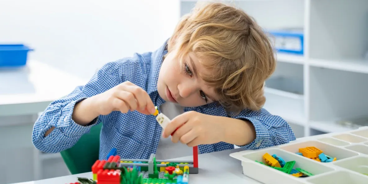 Хлопчик уважно збирає конструктор за столом у світлій кімнаті